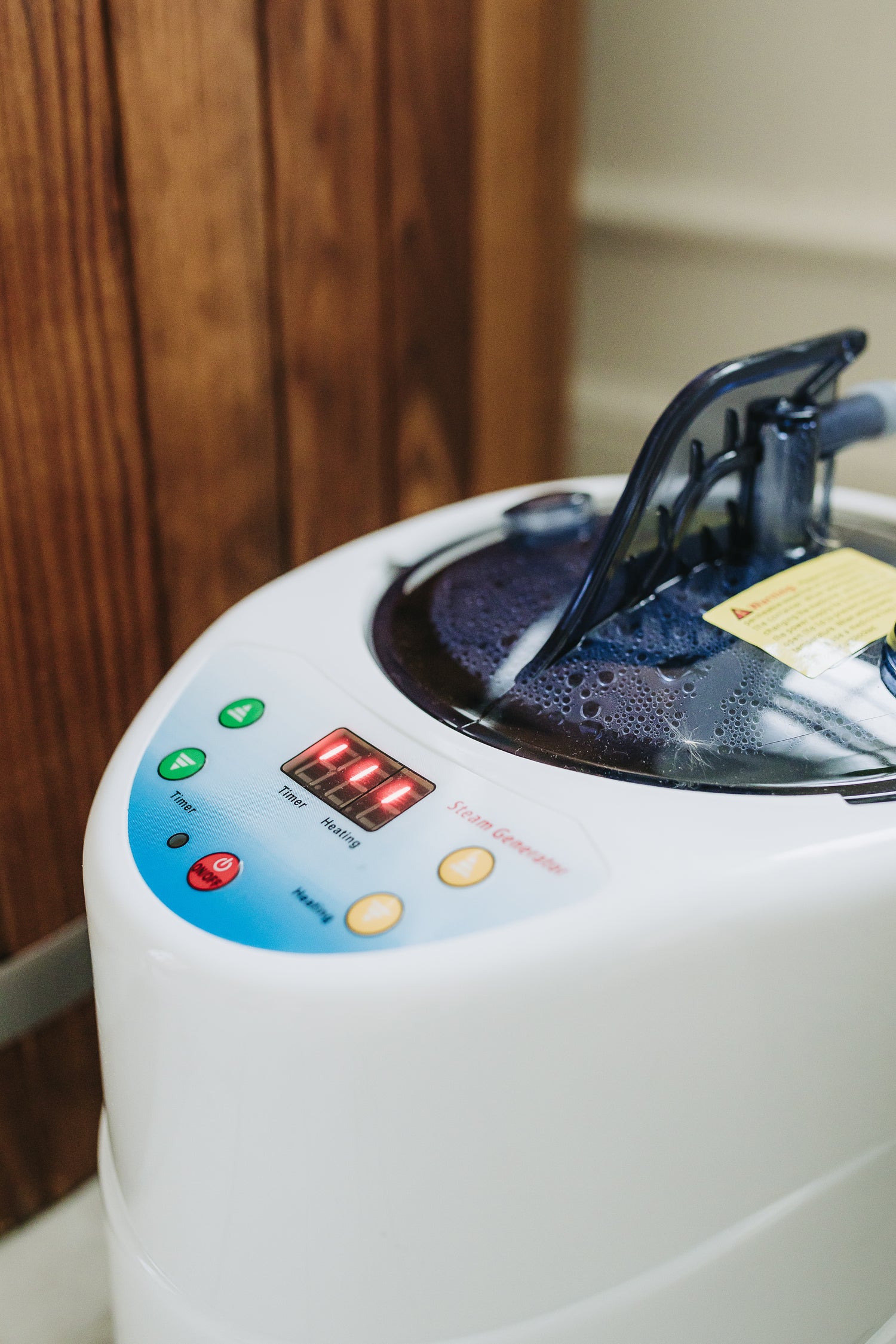 Close-up van een stoommachine met waterreservoir en bedieningsknoppen naast een houten stoomsauna