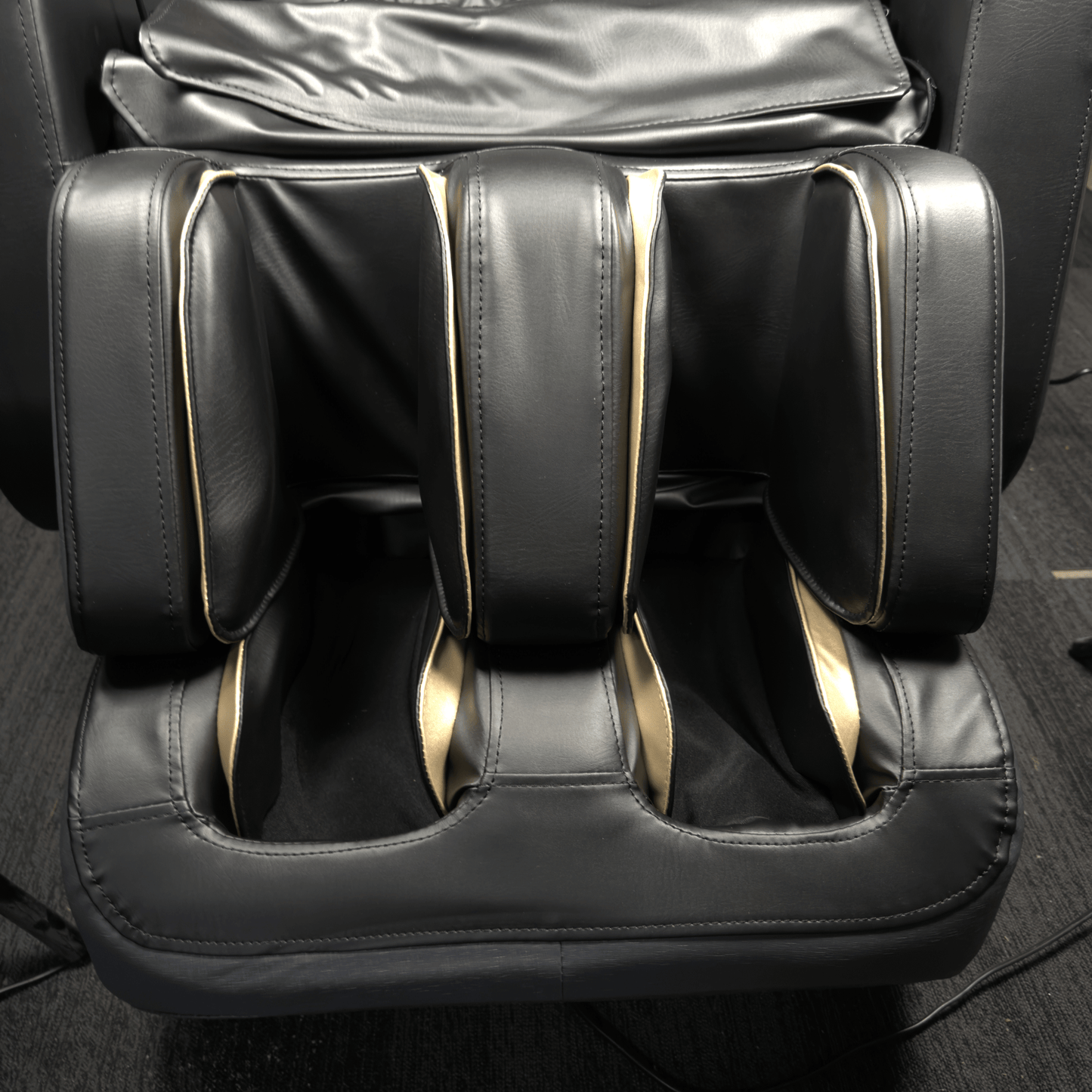 close-up van zwart voet en kuitgedeelte van massagestoel met goudkleurige accenten