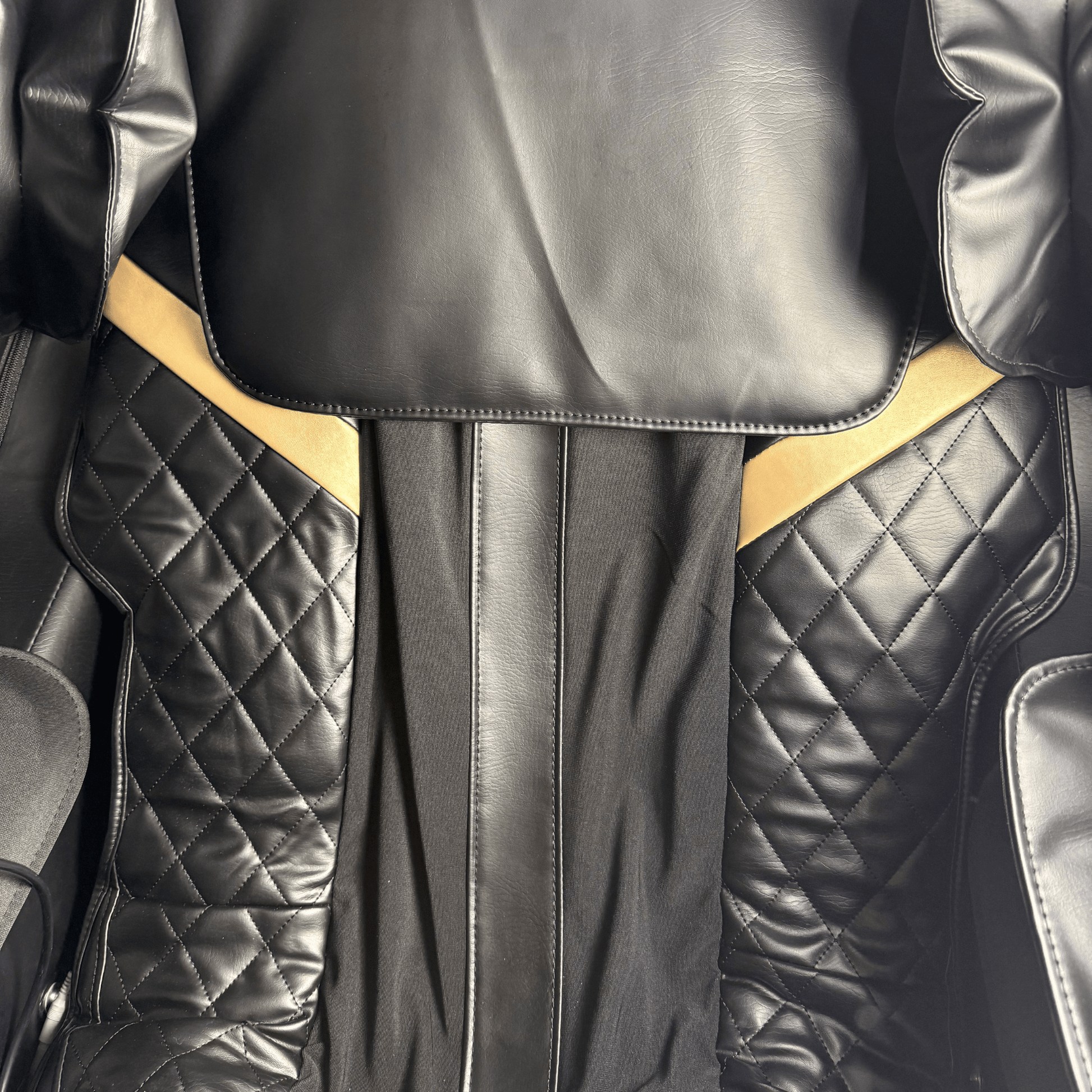 close-up van zwarte quilted rugleuning van massagestoel met goudkleurige accenten