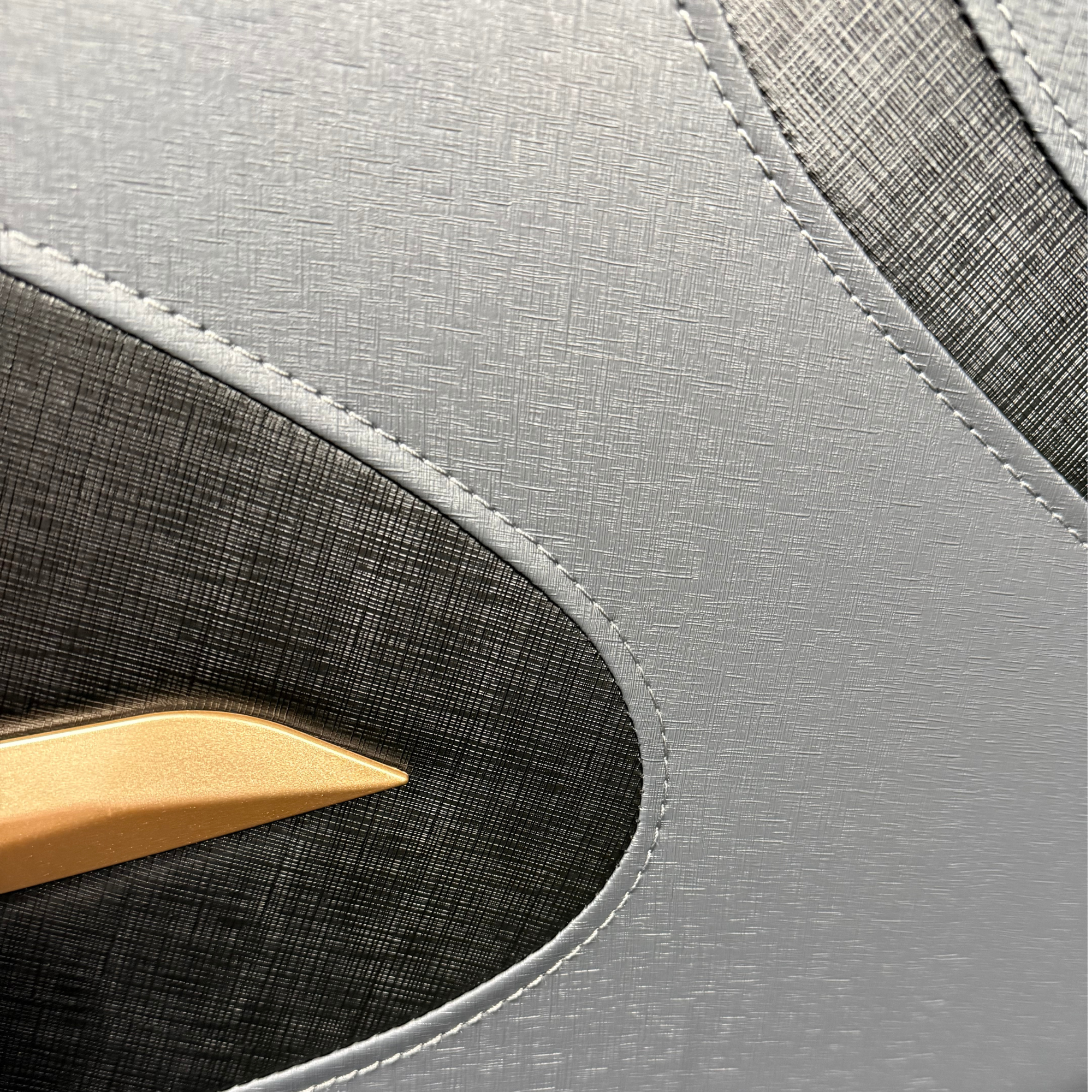 Detail van massagestoel met grijs en zwart kunstleer, zichtbare stiksels en goudkleurig accent